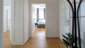 Un couloir au plancher de bois menant à une chambre à coucher équipée d’un lit et d’une table de chevet.