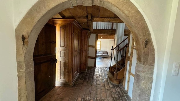 A narrow hallway with a stone archway, wooden doors, and a staircase leading to an upper level.