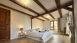 A bedroom with a large bed, wooden beams, a window, and a door.