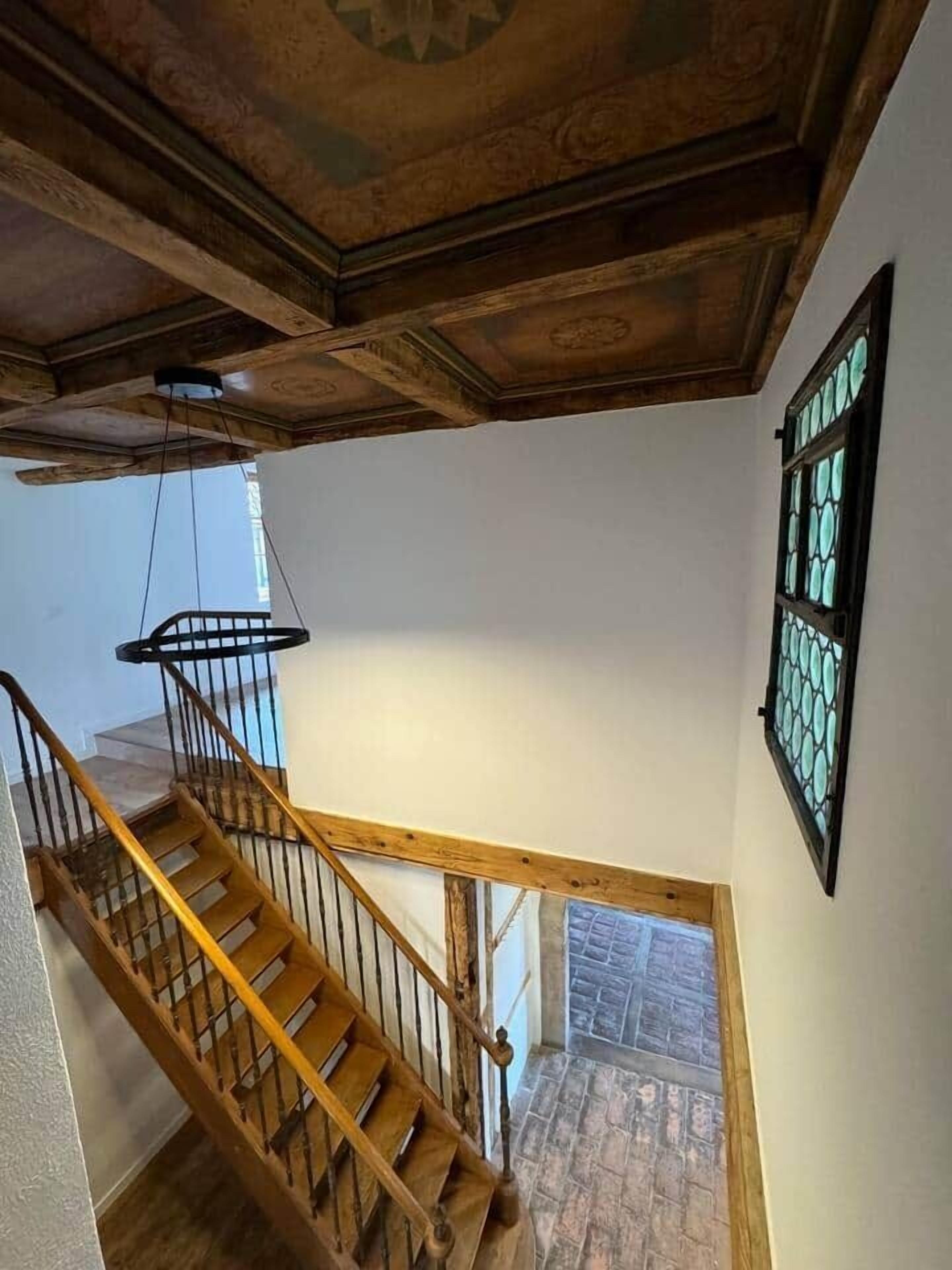 A wooden staircase with a wrought iron railing leading to a stone-tiled floor.