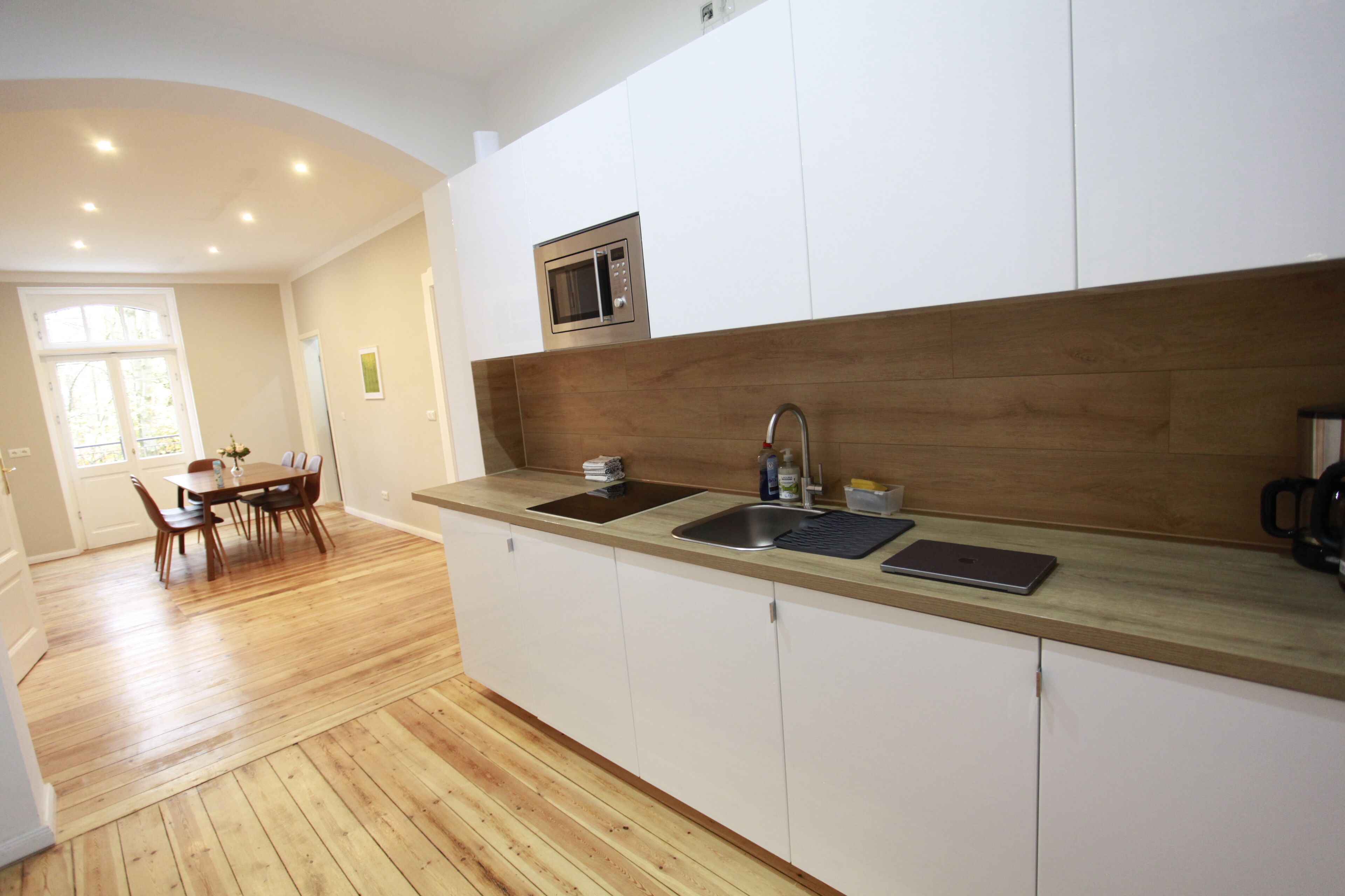 A modern kitchen with wooden flooring, white cabinets, a built-in microwave, and a sink.