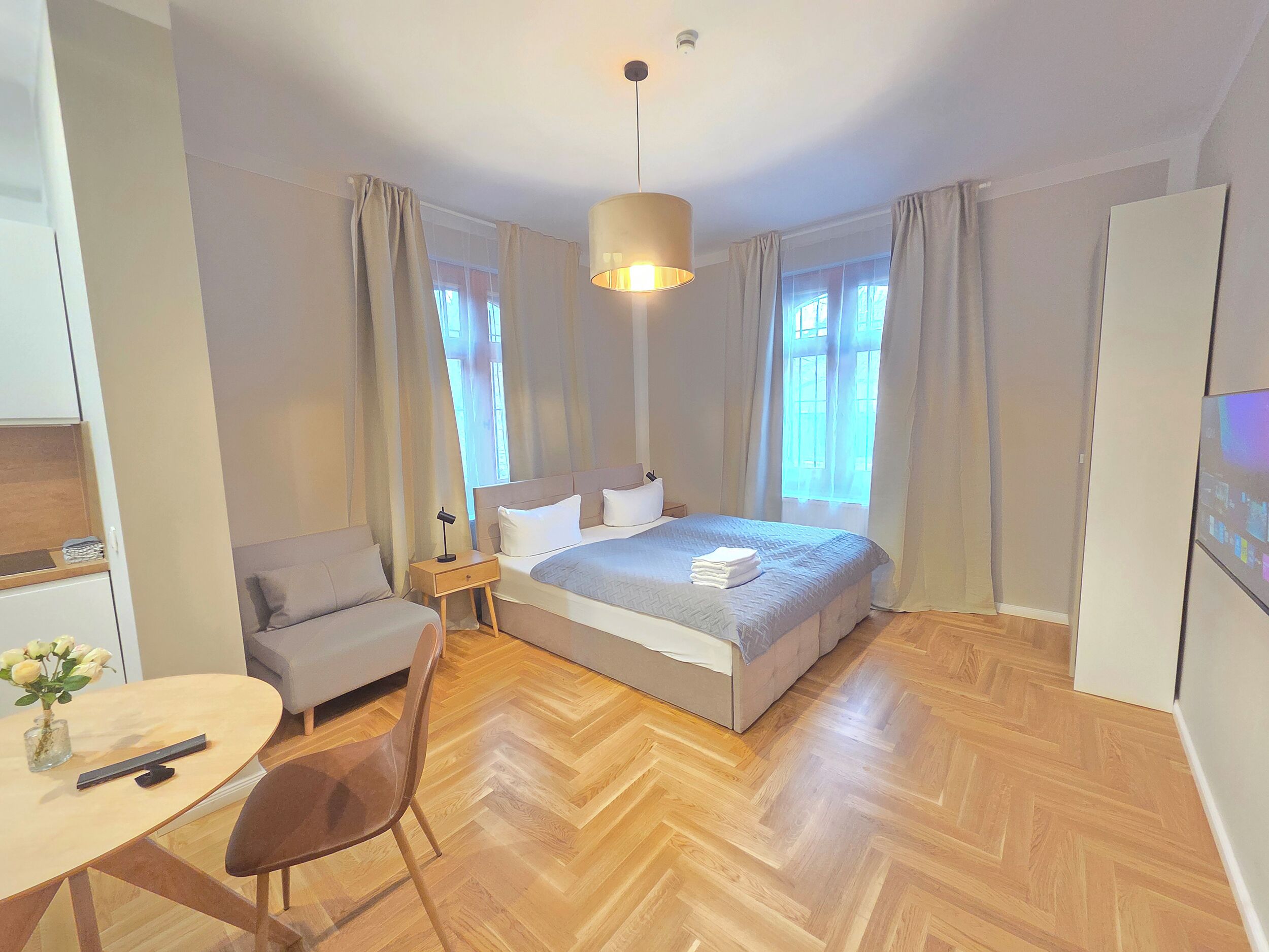 Une chambre d’hôtel moderne avec un grand lit, un bureau avec une chaise, une petite table ornée d’un vase de fleurs et un téléviseur.