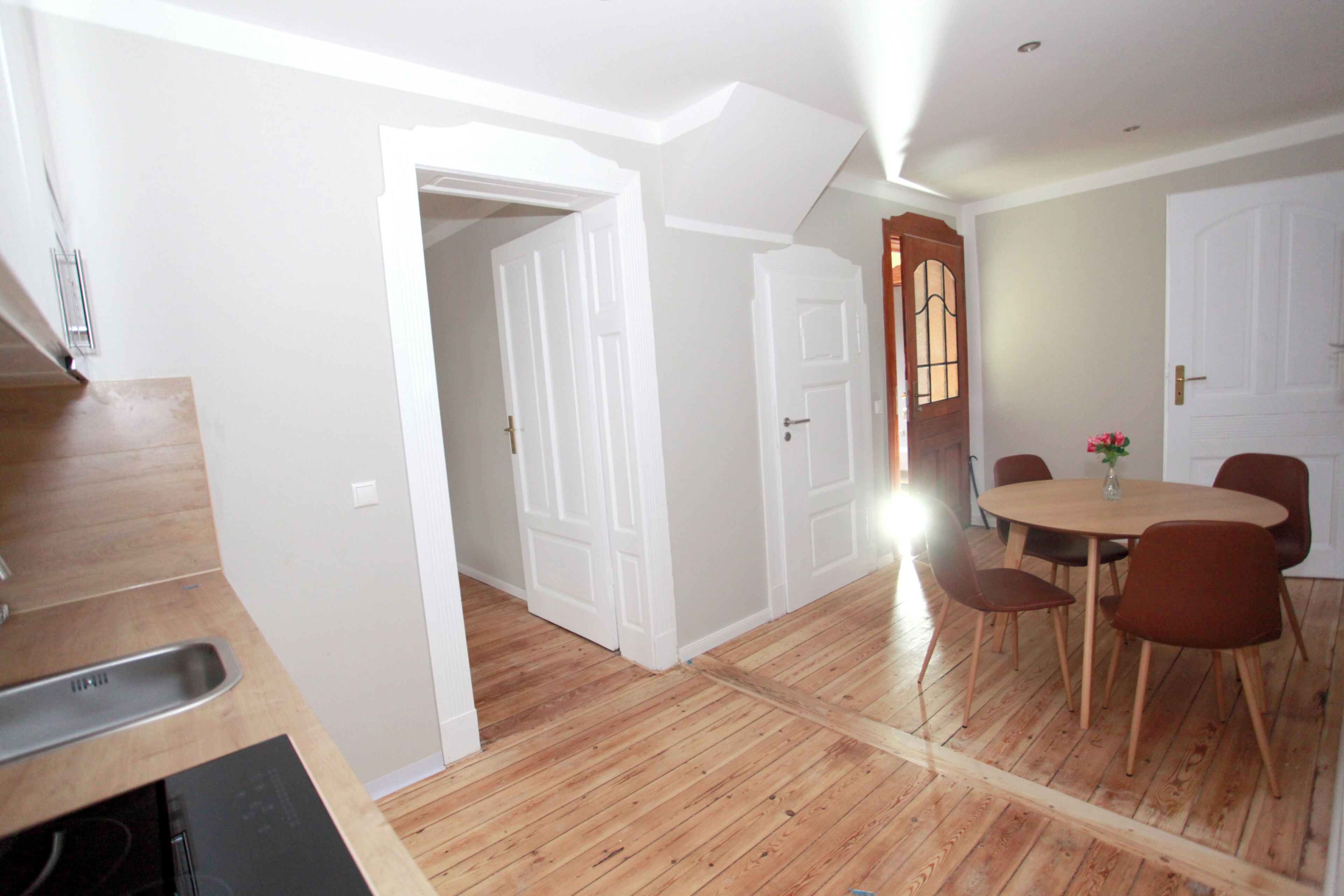 A dining area with a round table and six chairs, a wooden floor, and white walls.