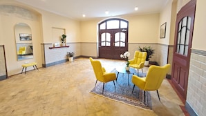 Una habitación amplia con un gran arco de entrada, sillas amarillas alrededor de una mesa pequeña y suelo de baldosas.