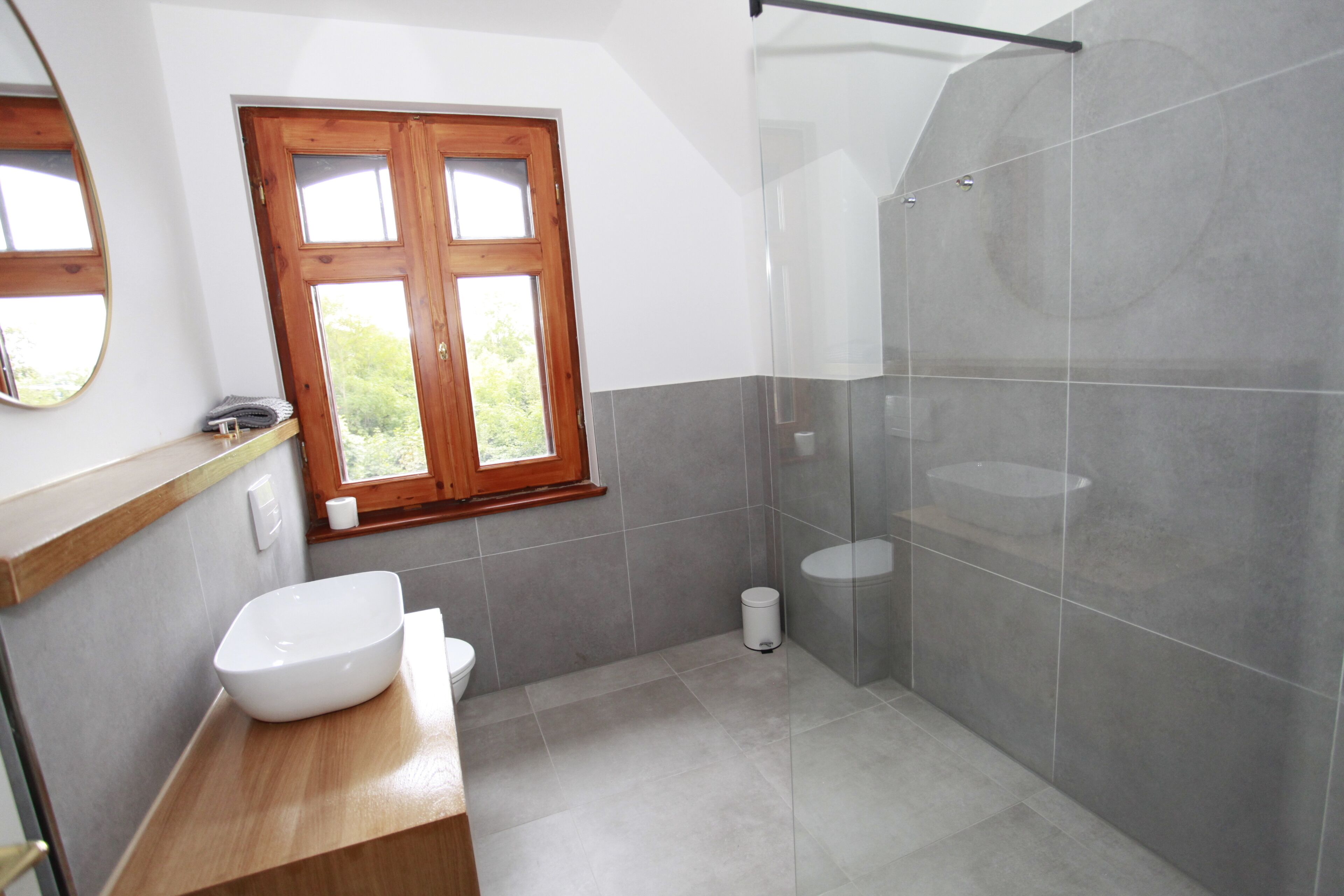 Un bagno moderno con un mobile vanitario in legno, un ampio specchio, una finestra e uno schermo doccia in vetro.