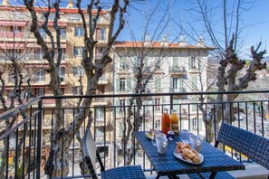 A balcony with a table set for two, featuring croissants and a bottle of orange juice.