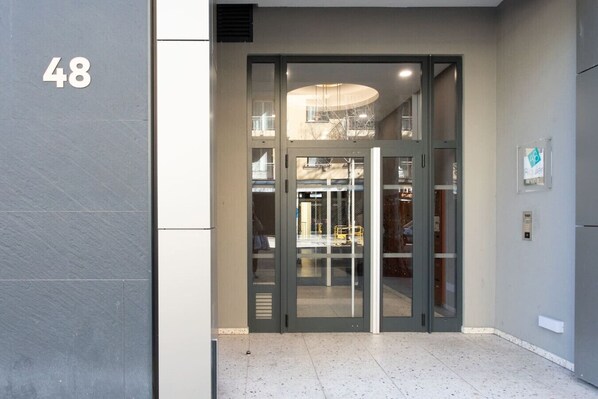 A modern building entrance with a glass door, a visible interior with a circular light fixture, and a number '48' on the wall.