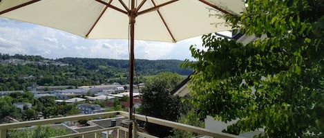 A balcony with a wooden floor, a wicker chair, and a large umbrella.
