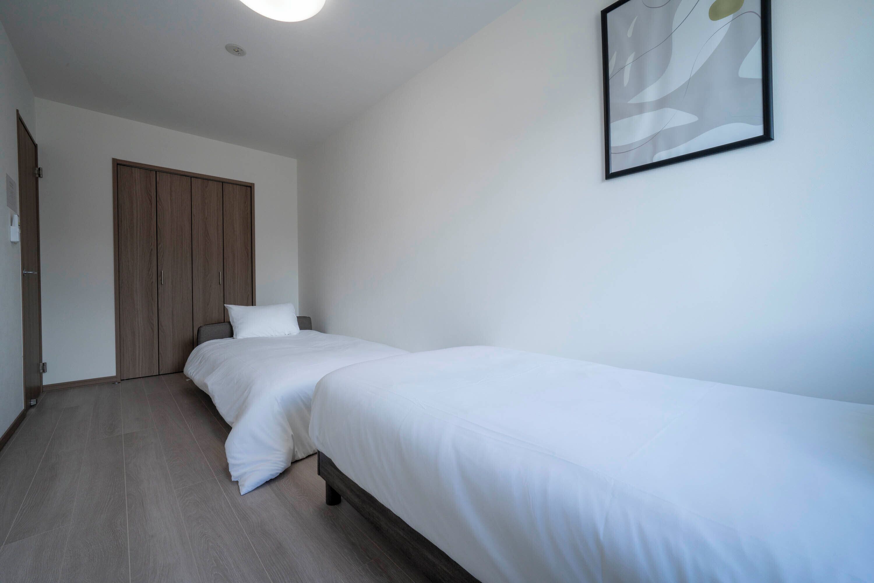 A bedroom with two single beds, a wooden wardrobe, and a framed abstract artwork on the wall.