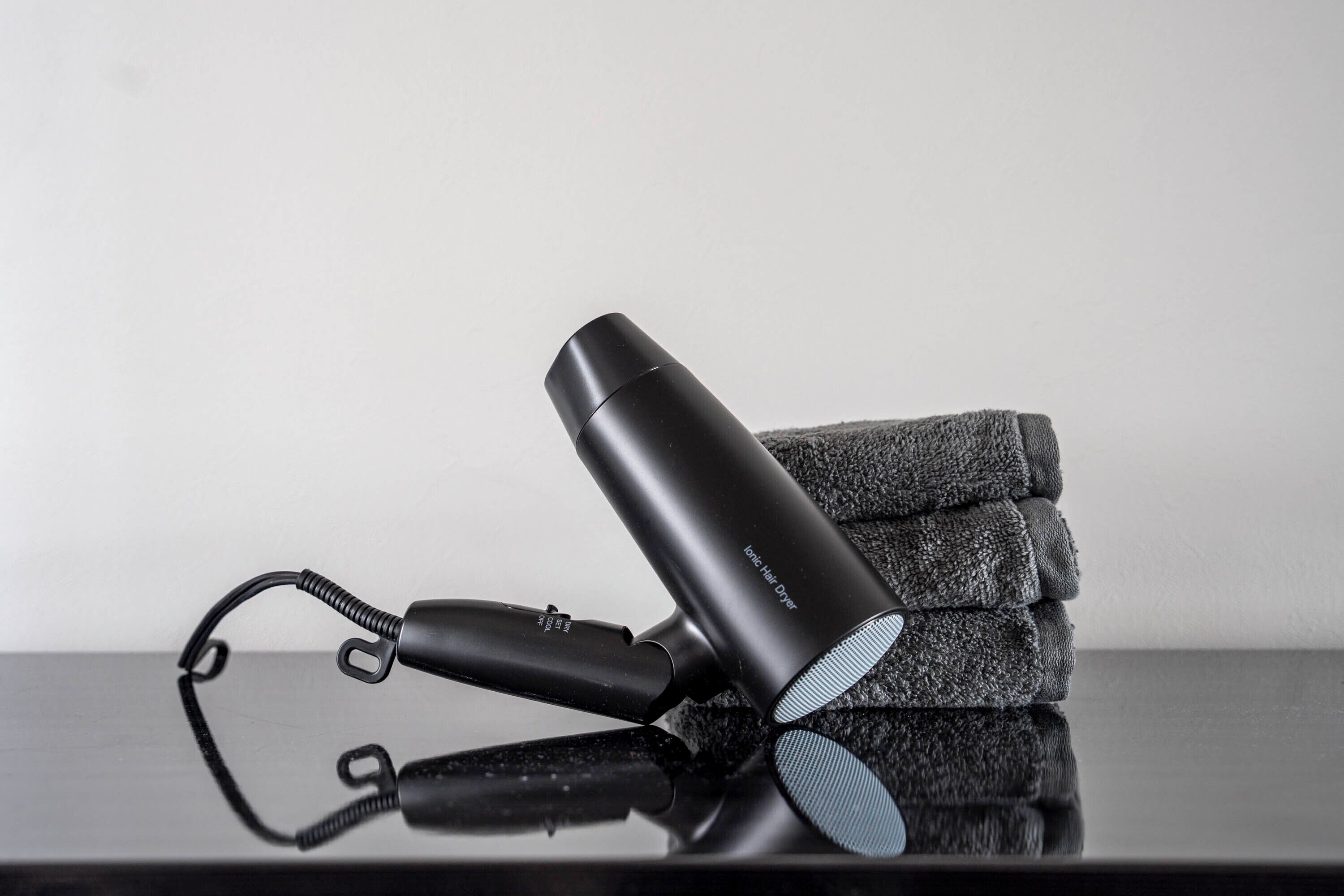 A black hair dryer and a folded towel on a reflective surface.