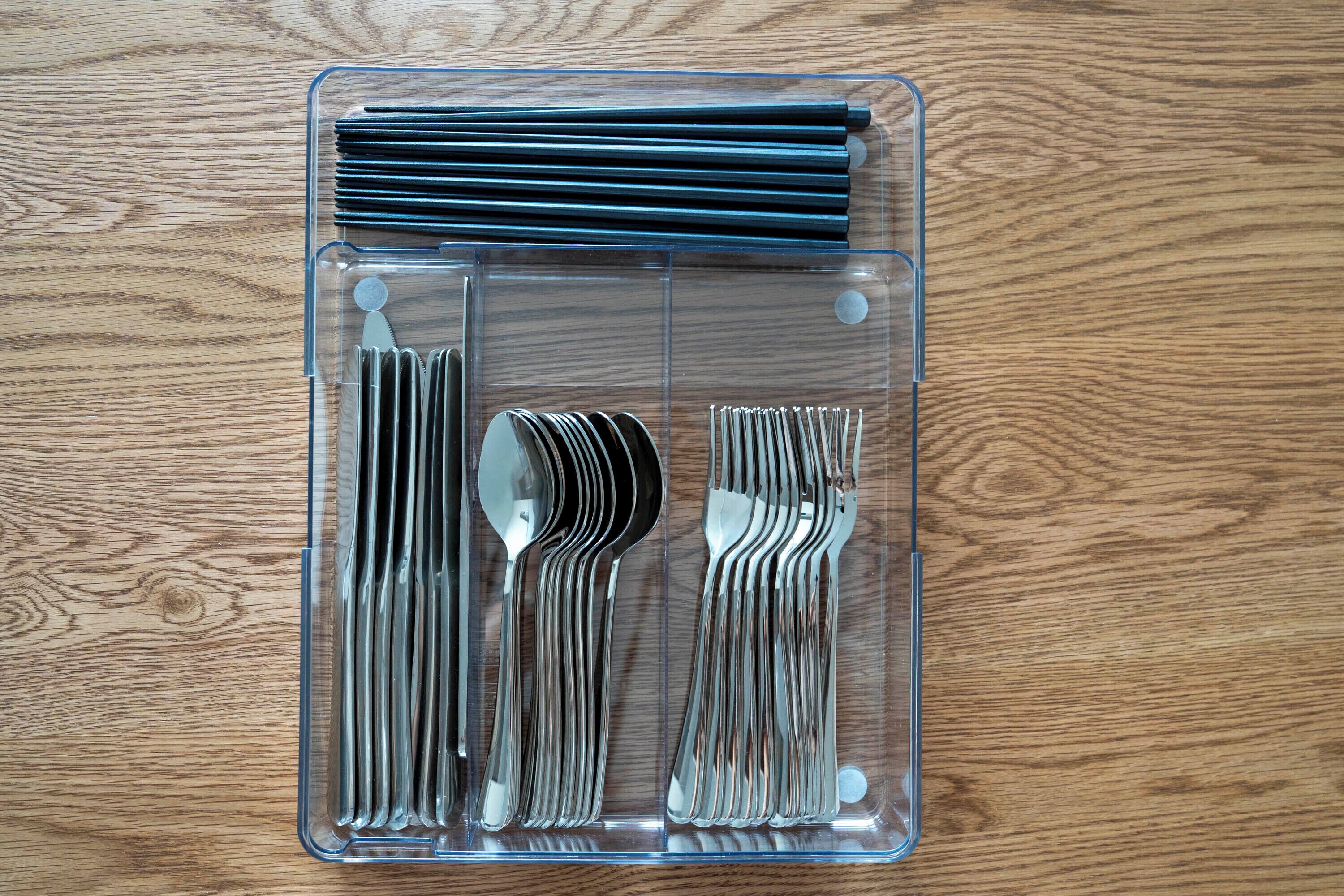 A clear plastic organizer with utensils and chopsticks on a wooden surface.