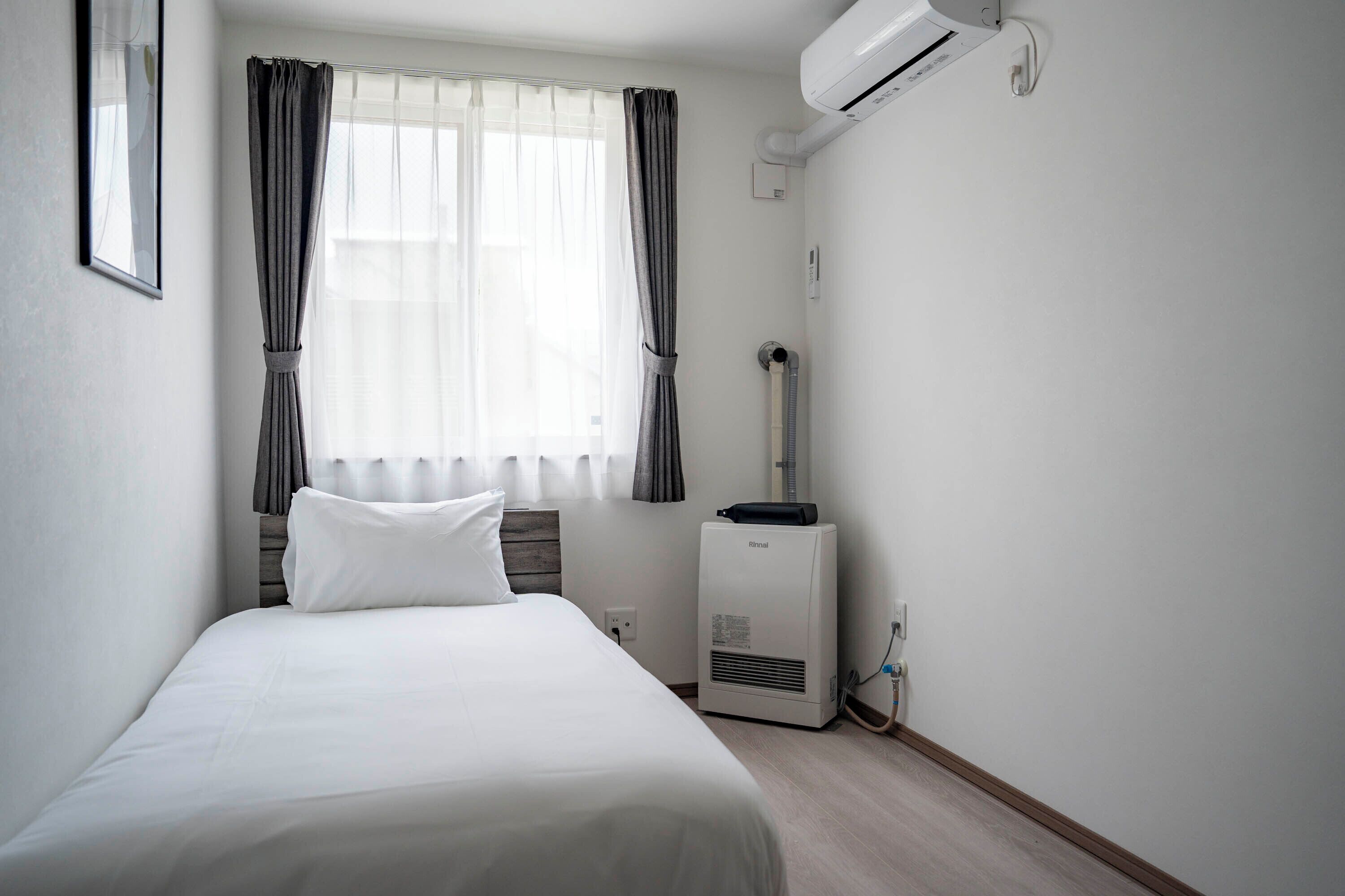A hotel room with a bed, air conditioning unit, and a window with curtains.
