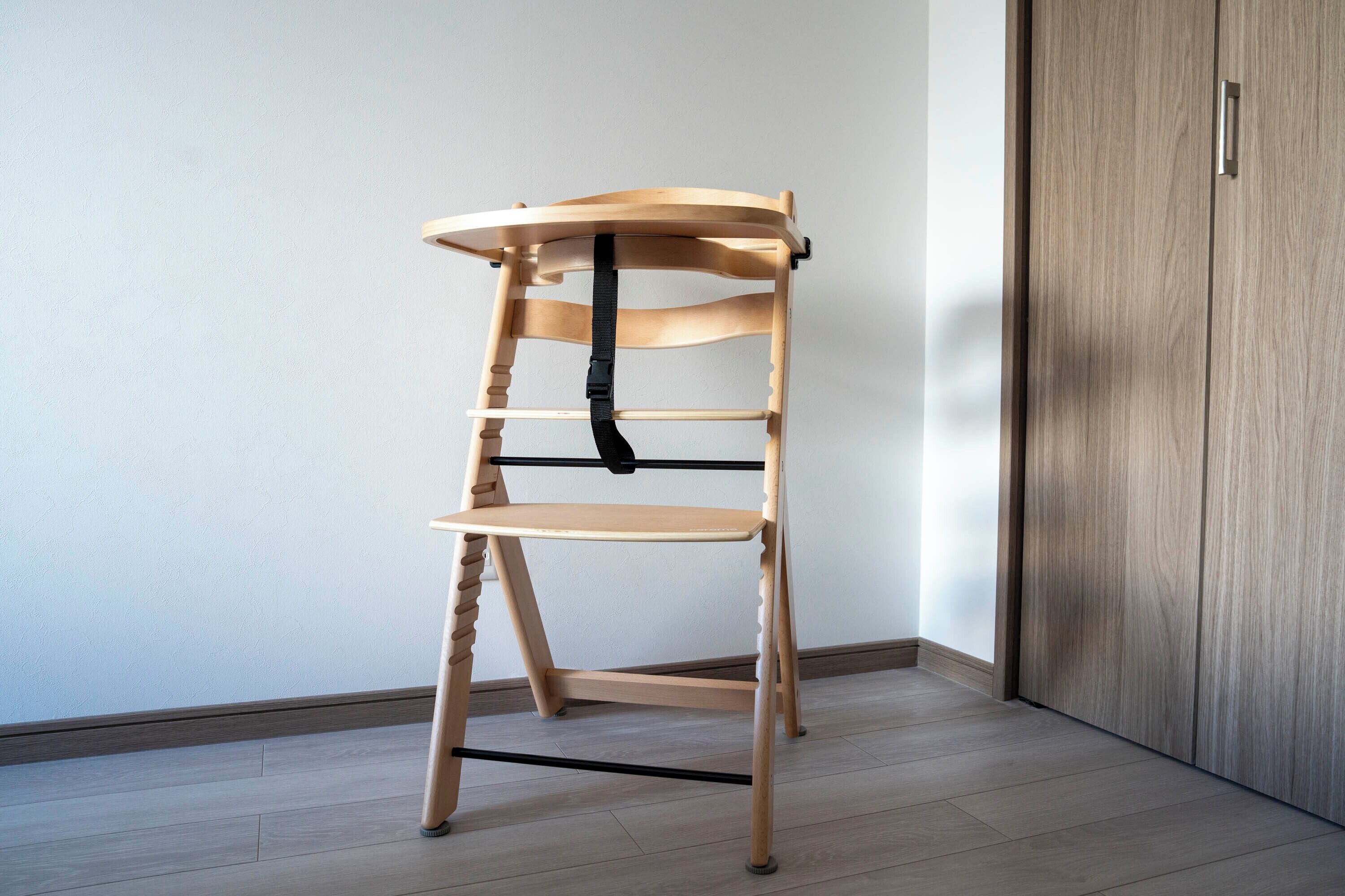A wooden chair with a black strap, placed against a wall with a wooden door.
