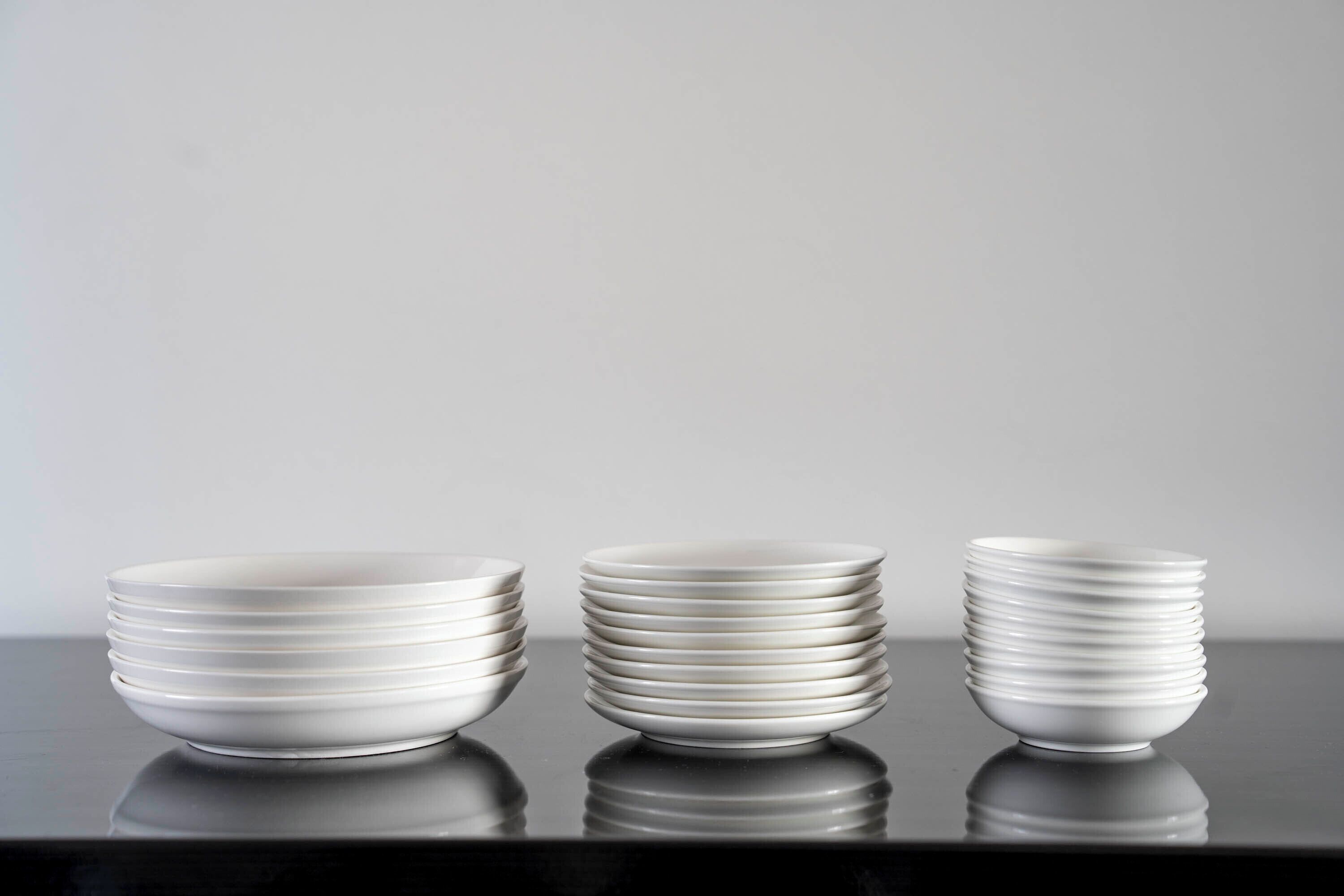 Trois piles d’assiettes blanches posées sur une surface noire réfléchissante.