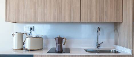 A modern kitchen with wooden cabinets, a white countertop, a coffee maker, a kettle, and a sink.