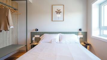 Una camera d'hotel con un letto, un comodino con una bottiglia e un bicchiere, un quadro appeso alla parete e una finestra.