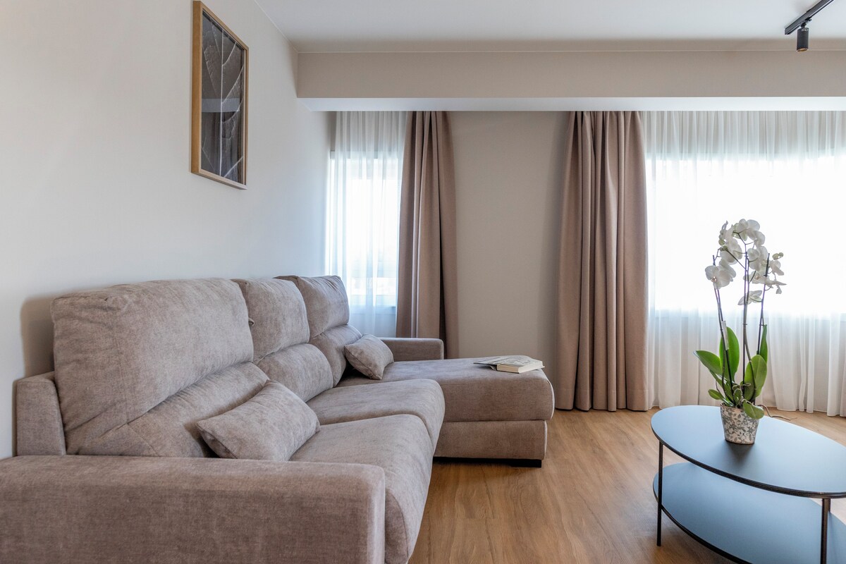 A modern living room with a sectional sofa, a small round table, and a potted plant.