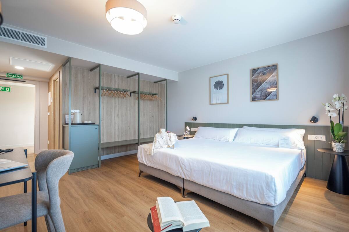 Ein Hotelzimmer mit Bett, Nachttisch, Sessel, Schreibtisch und Spiegel.