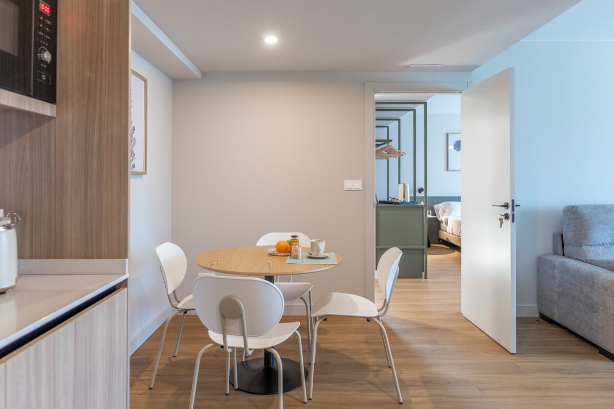 A modern kitchen with a microwave, a dining area with a round table and white chairs, and a grey sofa in a living area.