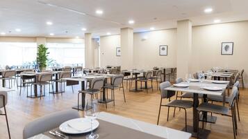 Un vaste espace dédié à la salle à manger, avec de nombreuses tables et chaises, de grandes fenêtres et un plafond doté d’un éclairage encastré.