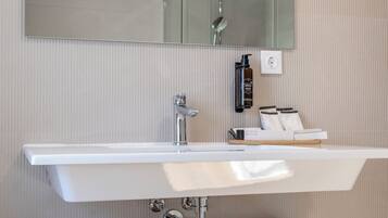 A bathroom with a large mirror, a white sink, a shower, and two towels on a shelf.