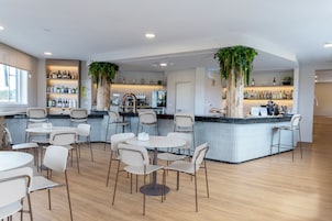 Een moderne barruimte met zitplaatsen en een bar, omringd door flessen op planken en een grote potplant.