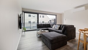 A modern living room with a sectional sofa, a round coffee table, and a wooden dining table. - Spacious 3 Bedroom Townhouse - Close to Stadium (Christchurch)