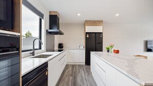 A modern kitchen with white cabinets, a black stove, and a large window. - Spacious 3 Bedroom Townhouse - Close to Stadium (Christchurch)