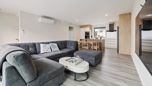 A modern living room with a grey sectional sofa, a white coffee table, and a wooden dining table with chairs. - Spacious 3 Bedroom Townhouse - Close to Stadium (Christchurch)