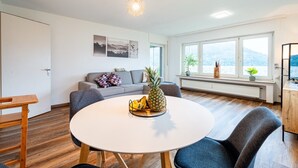 Ein modernes Wohnzimmer mit rundem Esstisch, grauem Sofa und Blick auf eine verschneite Landschaft durch große Fenster.