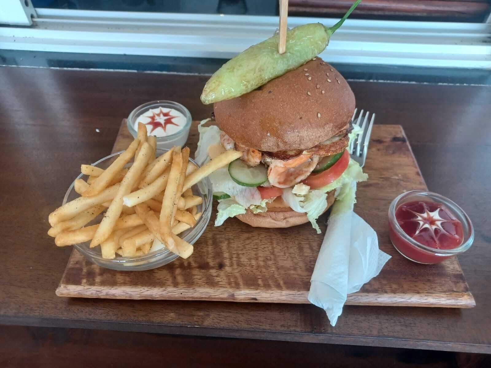Una hamburguesa con pepinillo, papas fritas y salsas sobre una mesa de madera.
