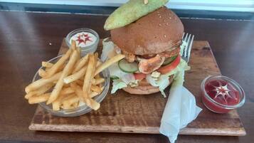 Una hamburguesa con pepinillo, papas fritas y salsas sobre una mesa de madera.