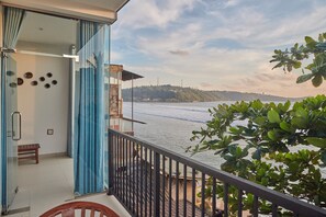 A balcony with a view of a body of water, a railing, and a door with curtains. - KINGS BAY BEACH RESORT (Galle)