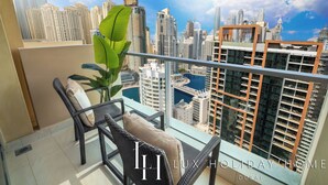 Un balcon agrémenté de meubles en osier, d’une plante en pot et offrant une vue sur les gratte-ciel de Dubaï.
