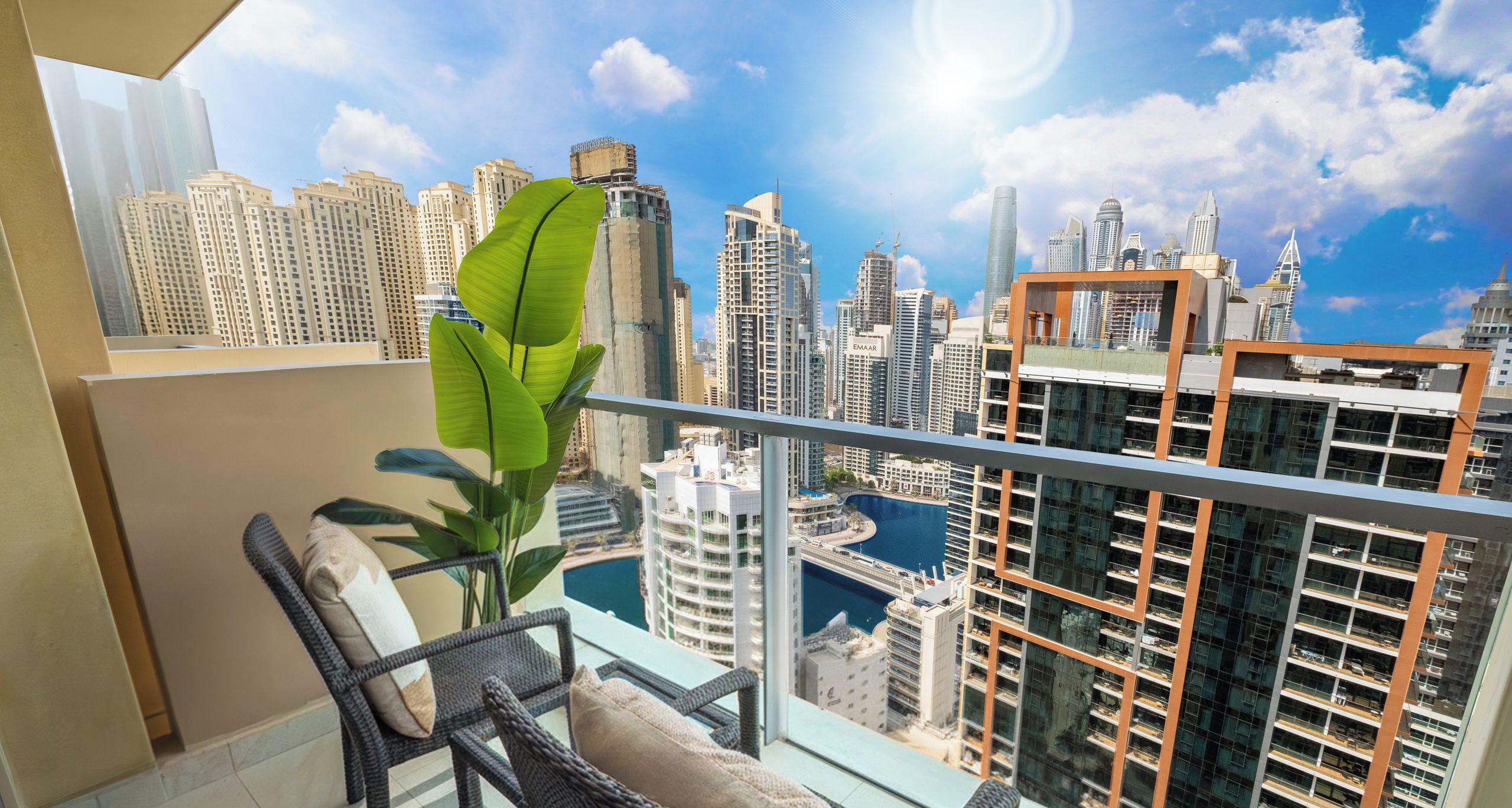 A balcony with wicker furniture, a potted plant, and a city view of Dubai's skyline.