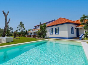 A poolside view of a house with a tiled roof, a swimming pool, and outdoor seating.