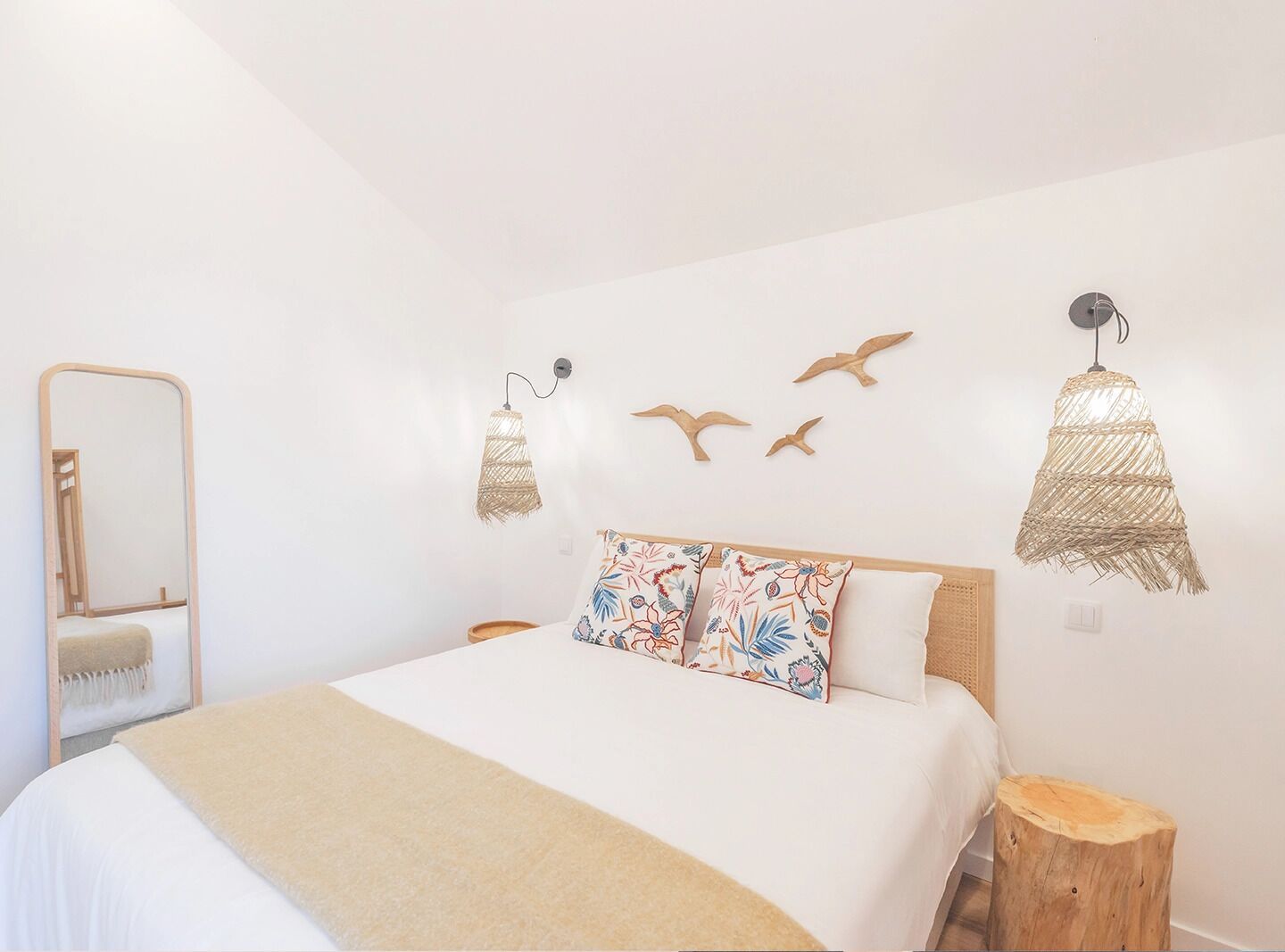 A bedroom with a bed, a mirror, wall-mounted lights, and decorative wall art.