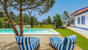 A poolside area with two striped lounge chairs, a swimming pool, and a house with blue windows and a red roof. - Almaa da Ria (Ilhavo)