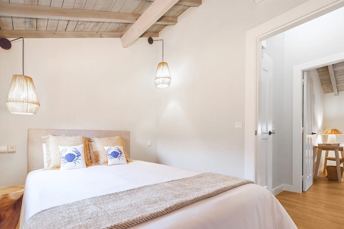 A bedroom with a large bed, two hanging lamps, and a wooden floor.