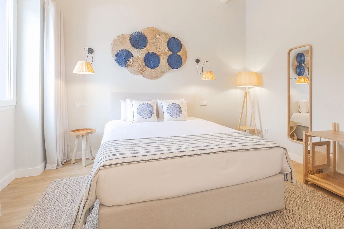 A neatly arranged bedroom with a large bed, bedside lamps, a mirror, and a small table.
