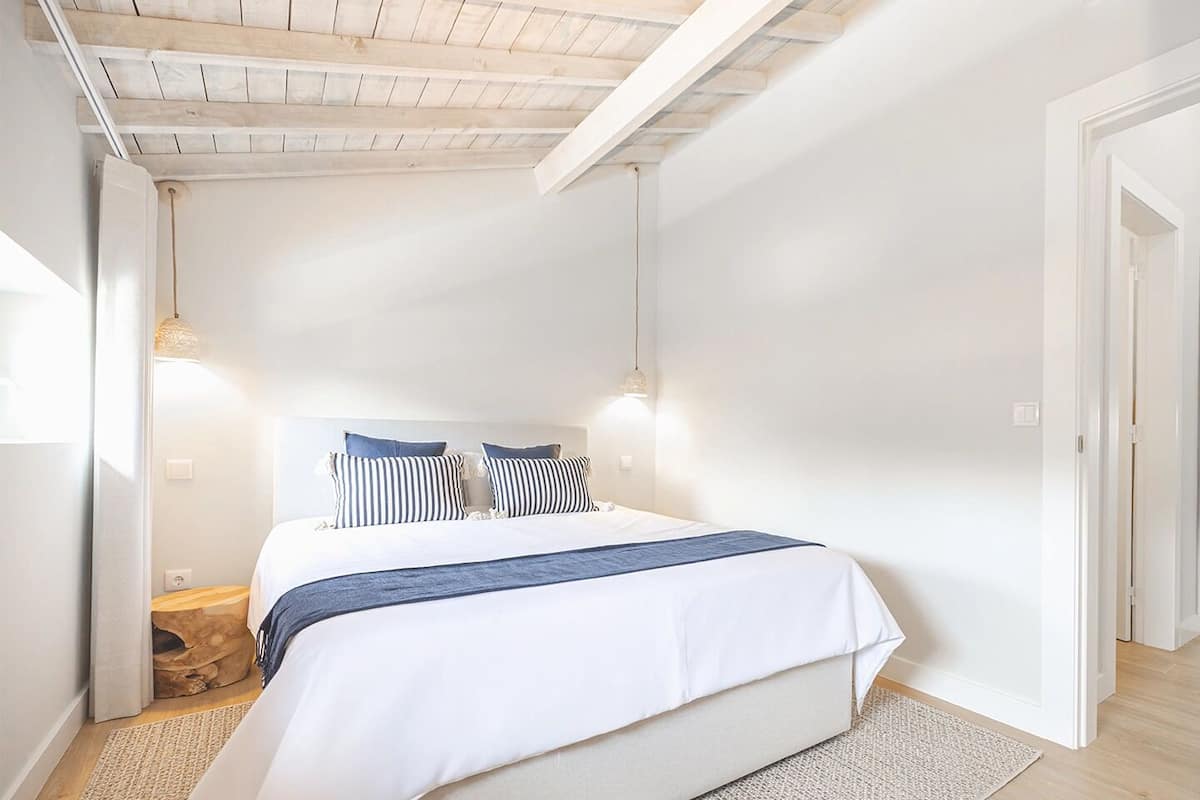 A bedroom with a bed, two bedside tables, a wooden headboard, and a sloped ceiling with exposed beams.