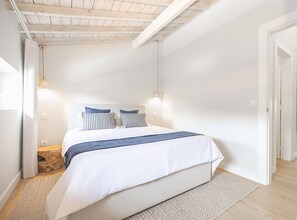 A bedroom with a bed, two bedside tables, a wooden headboard, and a sloped ceiling with exposed beams.
