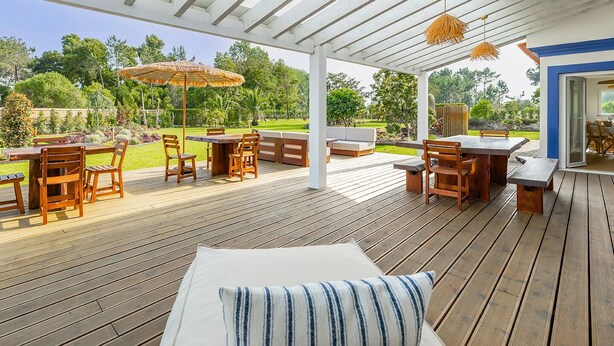 A covered outdoor deck with wooden furniture, including tables and chairs, and a thatched umbrella. - Almaa da Ria (Ilhavo)
