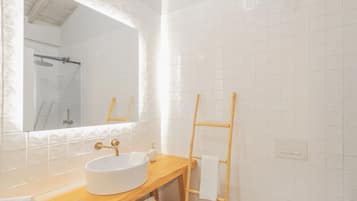 A bathroom with a round white sink, a wooden vanity, a mirror, and a towel rack.