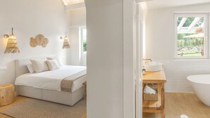 A modern bedroom with a large bed, bedside lamps, and a view of a garden through a window. - Almaa da Ria (Ilhavo)