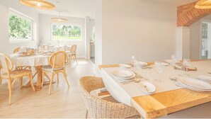 A bright dining area with wicker furniture and pendant lights, large windows offering a view of greenery. - Almaa da Ria (Ilhavo)