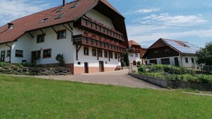 Un bâtiment traditionnel à plusieurs étages, doté d’un toit en pente, de balcons ornés de jardinières et de panneaux solaires.