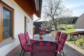 Een terras met een tafel en stoelen, een plant in pot, en uitzicht op een groen landschap.