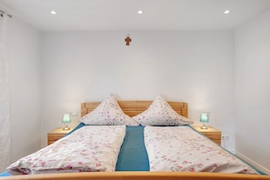 Een bed met bloemenbedekking, twee bedlampen en een houten hoofdbord.