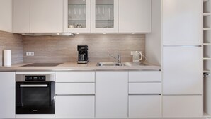 Une cuisine moderne avec des meubles blancs, un four encastré, une machine à café et un évier.